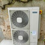 Installation d'une pompe à chaleur air-eau par PC Rénovation, vue devant un mur, sous une vigne